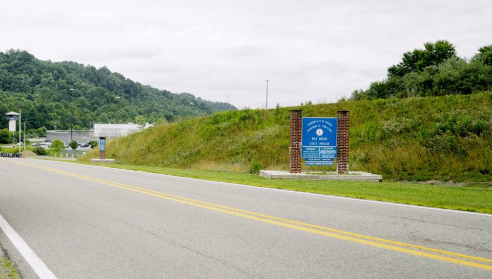 A view from the road of the blue sign for Red Onion State Prison in front of a green hill.