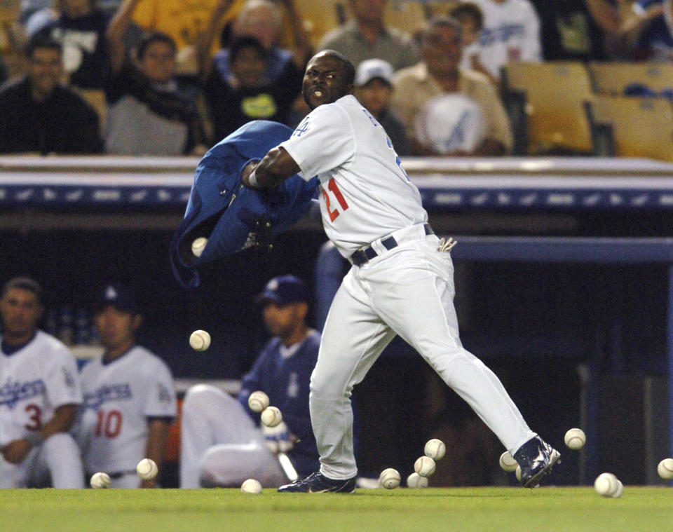 FILE - Los Angeles Dodgers' Milton Bradley throws a bag of baseballs onto the field after being ejected from the game by umpire Terry Craft for arguing balls and strikes in the sixth inning of a baseball game against the Milwaukee Brewers, June 1, 2004, at Dodgers Stadium in Los Angeles. Automatic balls and strikes could soon be coming to the major leagues. Disappearing with that are the complaints that an umpire’s strike zone was too wide or a pitcher was getting squeezed, followed by the helmet-slamming, dirt-kicking dustups that are practically as old as the sport itself. (AP Photo/Matt Brown, File)