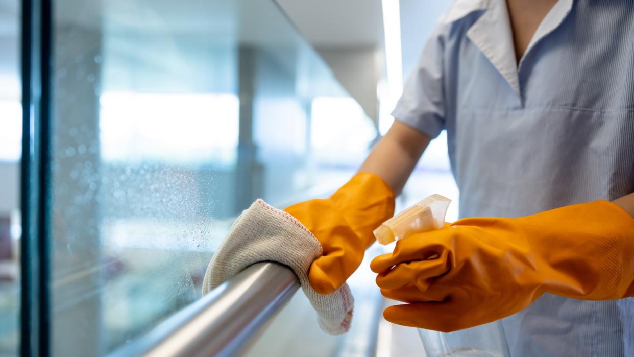  Close-up of cleaner spraying a handrail with disinfectant and cleaning it . 