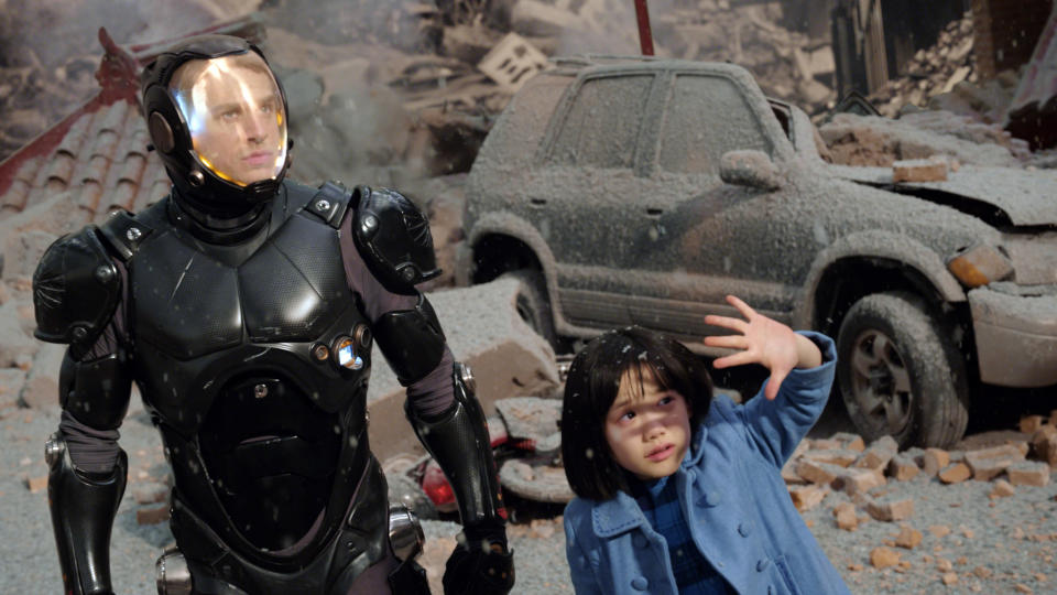 A man in robotic armor stands beside a frightened young girl