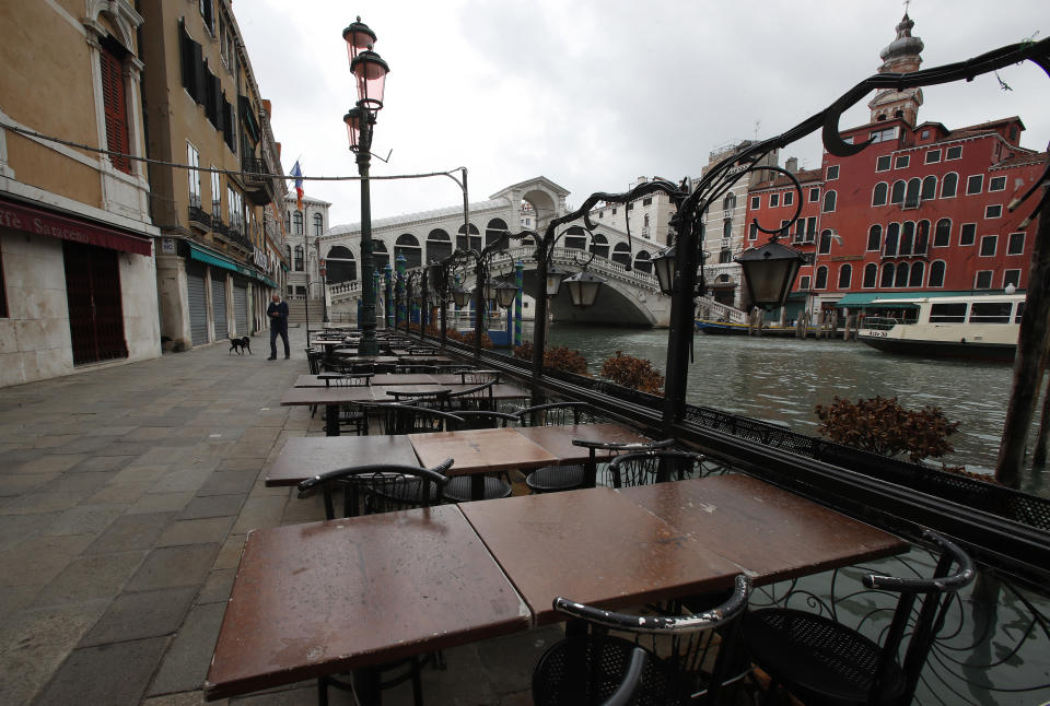 In this picture taken on Wednesday, May 13, 2020, a man wearing a sanitary mask walks his dog in Venice, Italy. Venetians are rethinking their city in the quiet brought by the coronavirus pandemic. For years, the unbridled success of Venice's tourism industry threatened to ruin the things that made it an attractive destination to begin with. Now the pandemic has ground to a halt Italy’s most-visited city, stopped the flow of 3 billion euros in annual tourism-related revenue and devastated the city's economy. (AP Photo/Antonio Calanni)