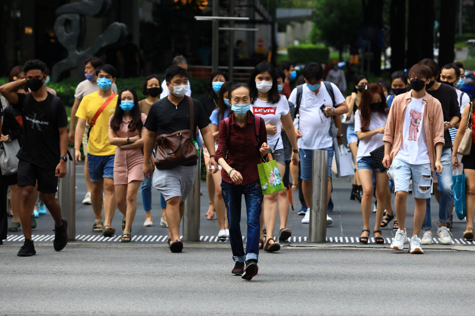 SINGAPORE - JUNE 20:  People wearing protective masks cross a street at Orchard Road shopping belt on June 20, 2020 in Singapore. From June 19, Singapore started to further ease the coronavirus (COVID-19) restrictions by allowing social gatherings up to five people, re-opening of retail outlets and dining in at food and beverage outlets, subjected to safe distancing. Parks, beaches, sports amenities and public facilities in the housing estates will also reopen. However, large scale events, religious congregations, libraries, galleries and theatres will remain closed.  (Photo by Suhaimi Abdullah/Getty Images)