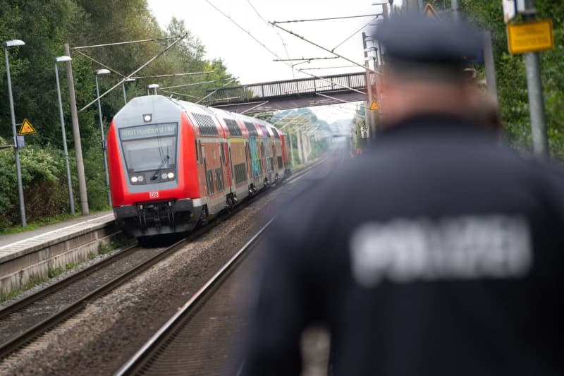 A police officer walks across a platform while in the background a double-decker Deutsche Bahn (DB) regional train pulls into the station. Jonas Walzberg/dpa