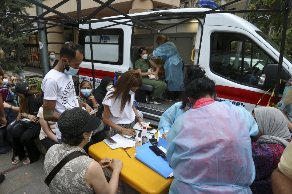 People, most of them residents of Iran stand in line for a vaccine at a mobile vaccination station in the center of Yerevan, Armenia, Wednesday, July 14, 2021. Hundreds of Armenians lined up in the streets of the Armenian capital to get free coronavirus shots, and some spent night on the streets to save on queueing. Under the Armenian government's directives effective since Friday, foreign nationals can only get AstraZeneca shots at five mobile vaccination points in Yerevan. (Vahram Baghdasaryan/PHOTOLURE via AP)