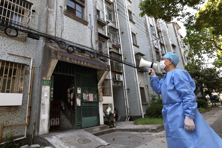 En esta foto publicada por la Agencia de Noticias Xinhua de China, un voluntario utiliza un megáfono para hablar con los residentes en cuarentena en un edificio de apartamentos en Shanghai, China, el martes 12 de abril de 2022. 