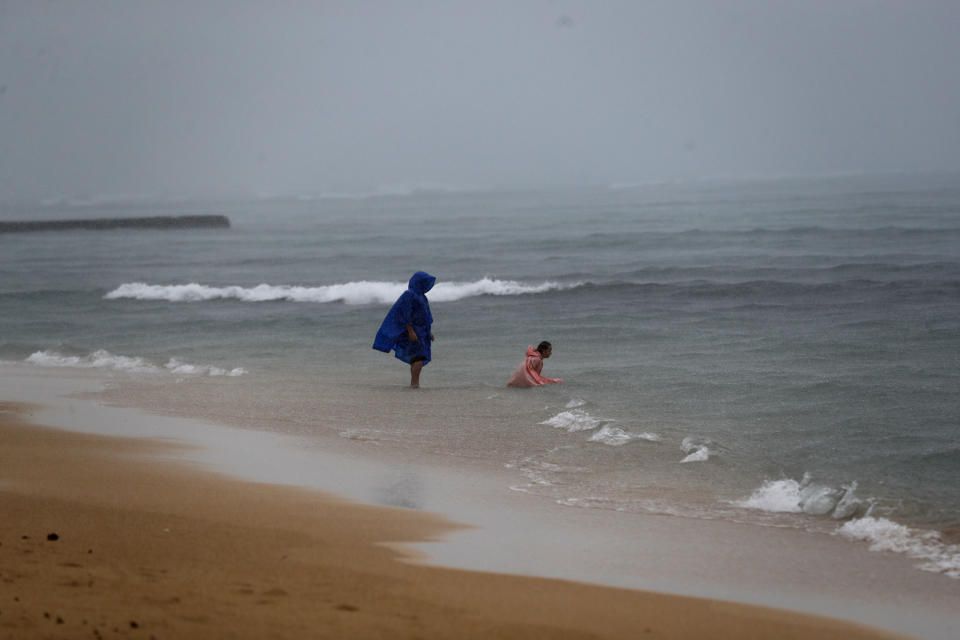 While wearing rain coats, beach goers play in the rain on Waikiki Beach, Monday, Dec. 6, 2021, in Honolulu. A strong storm packing high winds and extremely heavy rain flooded roads and downed power lines and tree branches across Hawaii, with officials warning Monday of potentially worse conditions ahead. (AP Photo/Marco Garcia)