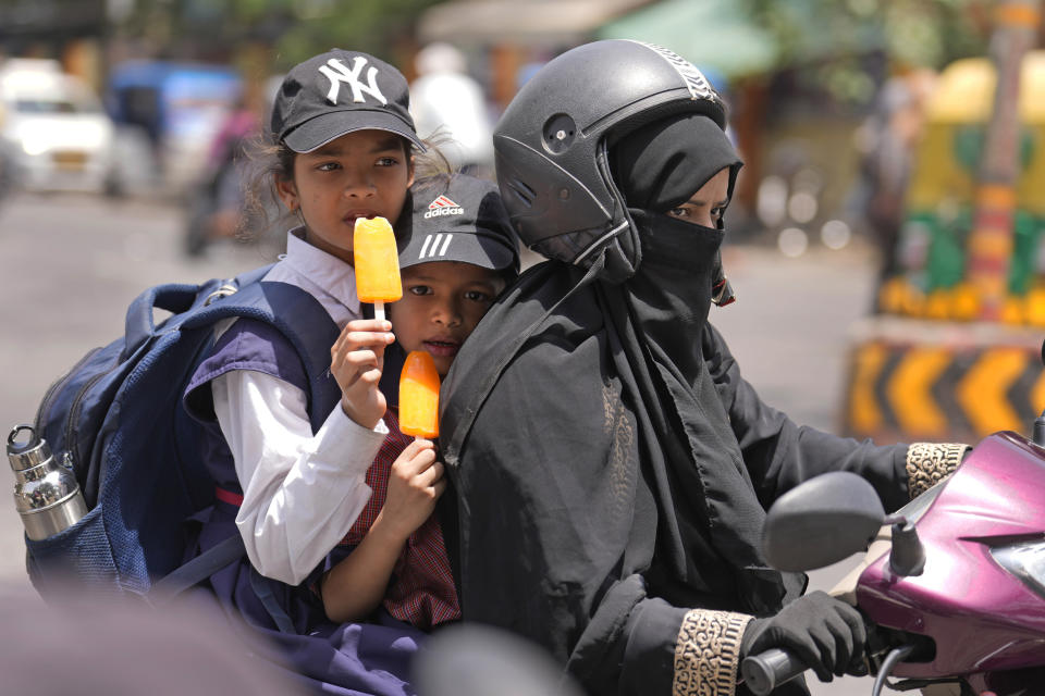 Schoolchildren eat ice lollies sitting on a scooter on a hot summer day in Lucknow, India, Friday, May 3, 2024. (AP Photo/Rajesh Kumar Singh)