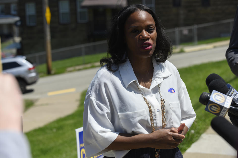 Summer Lee stands on a sidewalk and speaks before news microphones.