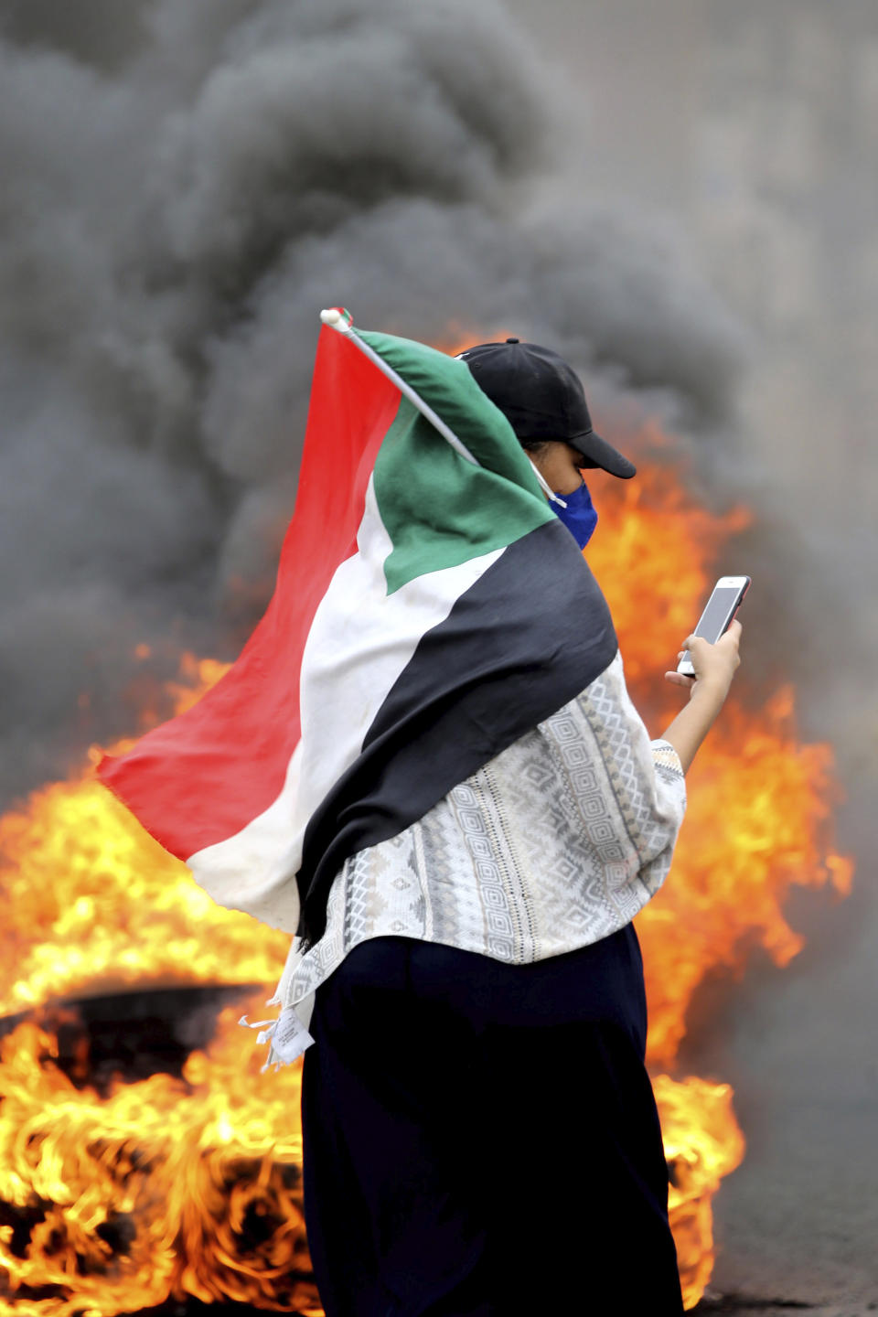A Sudanese woman carries a national flag during a demonstration to commemorate the first anniversary of a deadly crackdown carried out by security forces on protesters during a sit-in outside the army headquarters, in Khartoum, Sudan, Saturday, May 23, 2020. (AP Photo/ Marwan Ali)