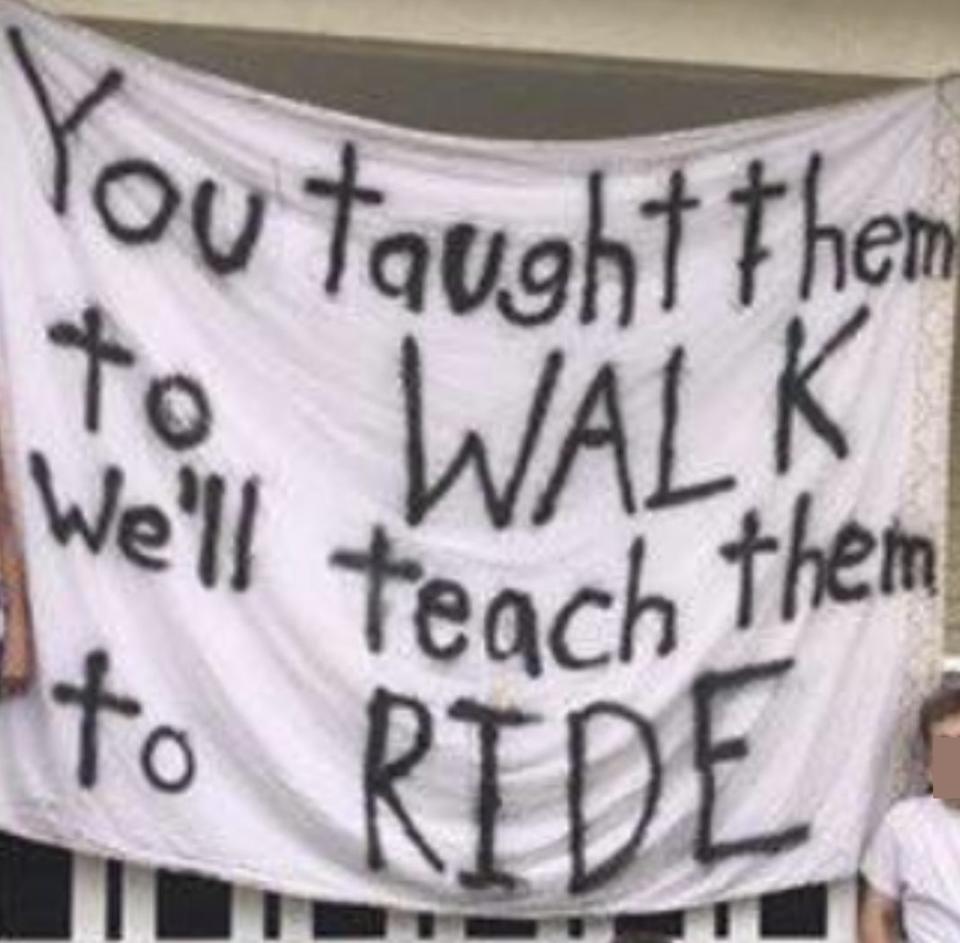 Members of a fraternity on the front lawn with a huge sign that says "you taught them to walk, we'll teach them to ride"