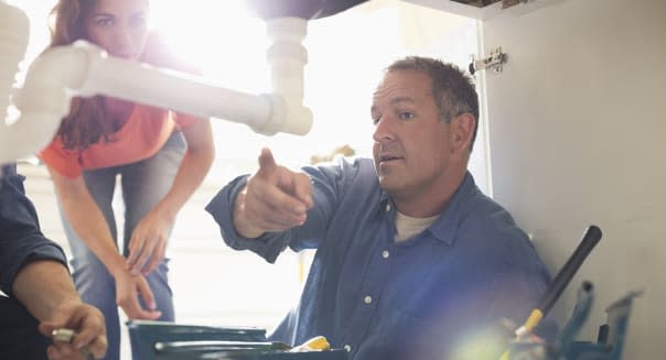 Plumbers working on pipes under sink