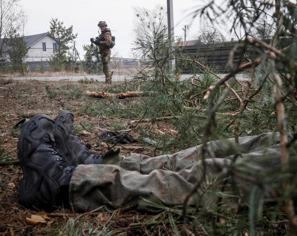 A Ukrainian service member stands near the body of a Russian soldier on the front line near Kyiv, as Russia's invasion of Ukraine continues, March 30, 2022. / Credit: GLEB GARANICH/REUTERS