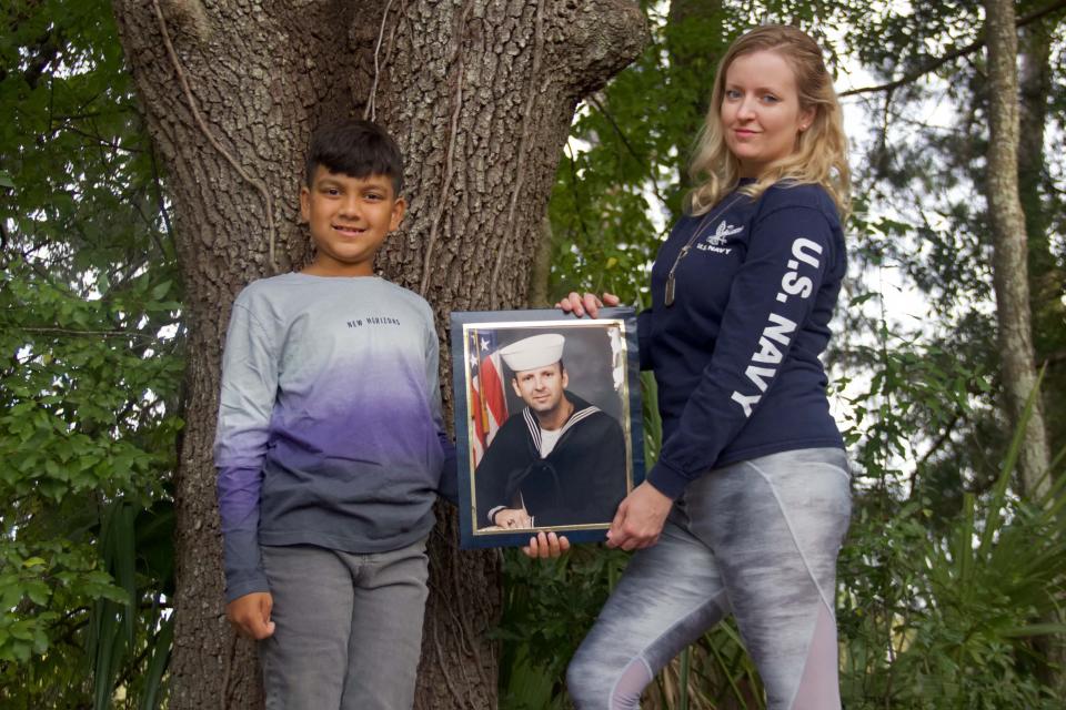 Luke Sukhram (left), 8, and his mother Sabrina Davis (right) stand with a photo of her father, Keith Davis, in Gainesville, Fla. on Monday, November 1, 2021. Davis was a United States Navy veteran who passed away in 2020 due to medical negligence. (Photo by Kiara Cline)