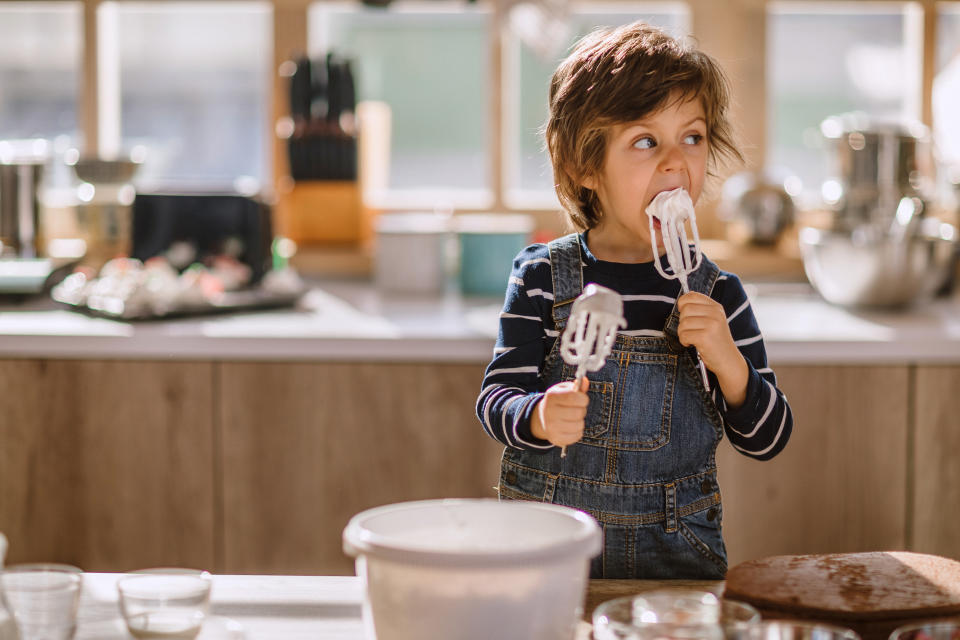 Cute Kid Tasting Whipped Cream of Egg Beater In Kitchen, Making Adorable Funny Faces in Manner of Sweet Taste