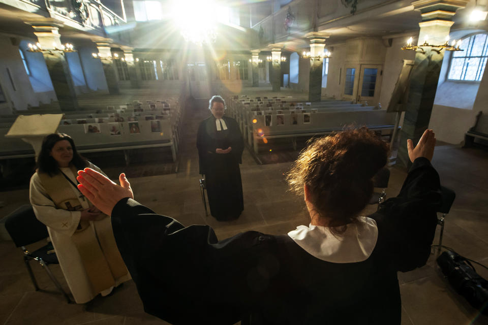 Vicar Kerstin Gommel, right, celebrates the Maundy Thursday Service besides Dean Jana Petri, left, and youth pastor Anna Boeck, center, in the empty Protestant church St. Marien in Suhl, Germany, Thursday, April 9, 2020. The church members are present symbolically with their portrait fixed to the pews. Due to the coronavirus no services are held these days. (AP Photo/Jens Meyer)