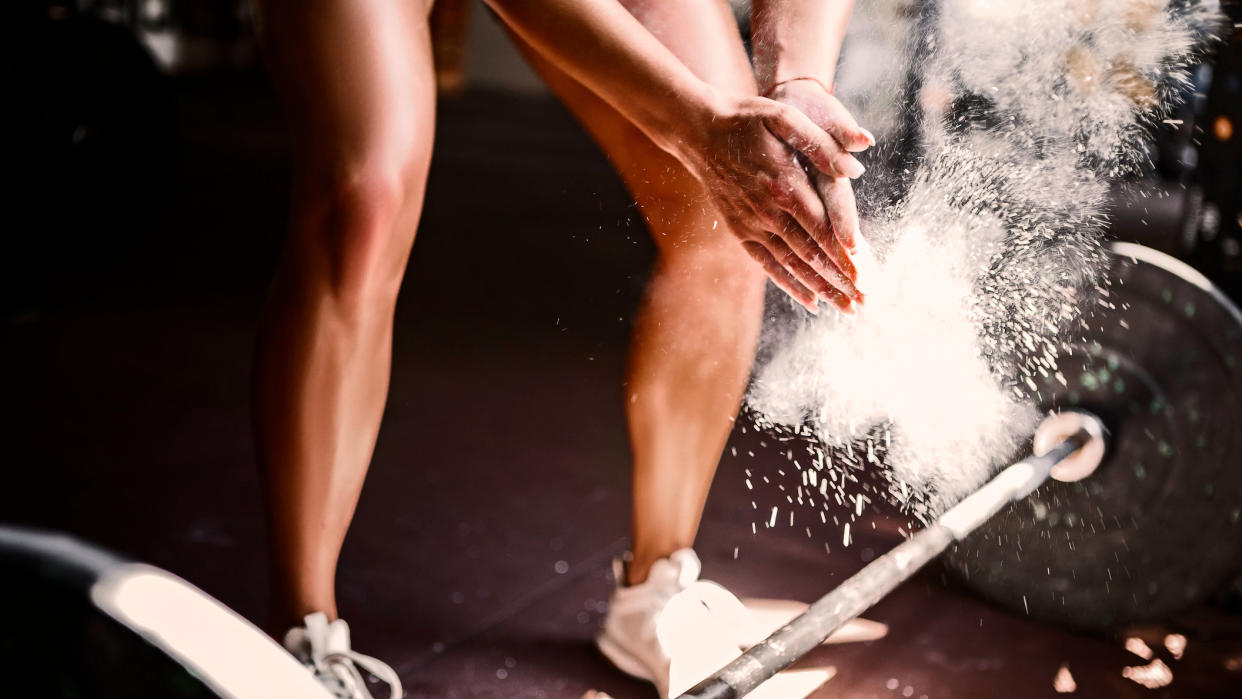  Woman stands over barbell and rubs chalk into her palms 