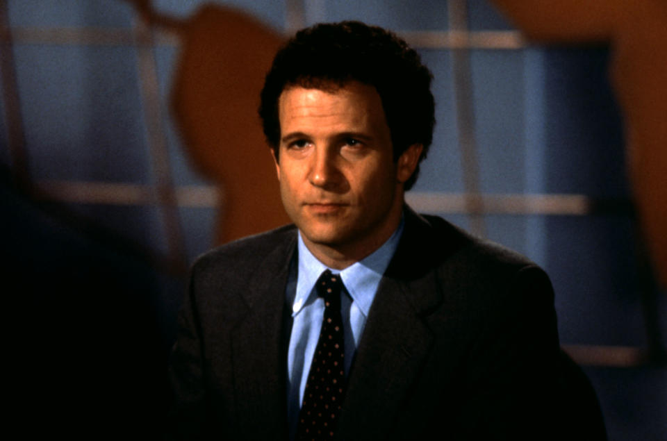 Albert Brooks sits at a news desk