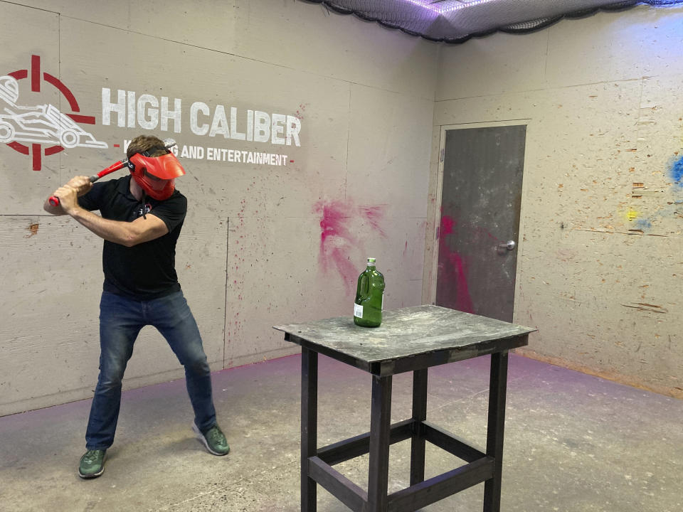 Jordan Munsters, co-founder and president of High Caliber Karting and Entertainment, begins his swing toward a glass bottle in one of the venue's "rage rooms," Monday, June 21, 2021, in Meridian Township, Mich. Michigan's coronavirus restrictions will be lifted starting Tuesday, allowing businesses to operate at 100% capacity. (AP Photo/David Eggert)