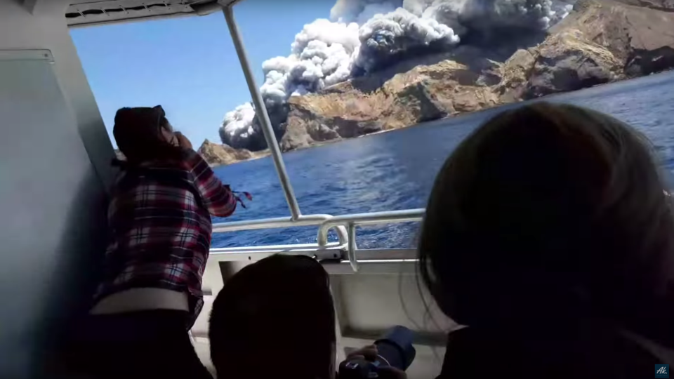 A tour group watches White Island erupt from a boat.