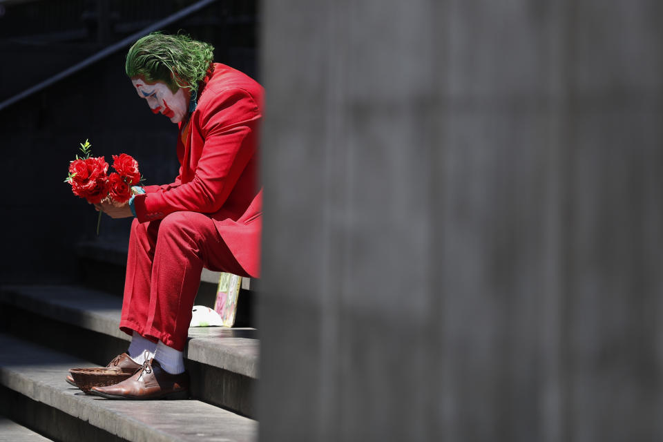 FILE - In this March 23, 2020 file photo, David Vazquez, a street performer dressed as the Joker, waits in hopes of pedestrians who will pay to take pictures with him in Mexico City. Vazquez, who also worked as a trainer in a gym until it shut down today, said business for street performers has plummeted, with the few clients still stopping opting to take their pictures from a distance or posing beside him awkwardly, amid the worldwide spread of the new coronavirus. "We have to pay rent, light, gas, telephone," said Vazquez. "Where will we get that money? We all want to work." (AP Photo/Rebecca Blackwell, File)