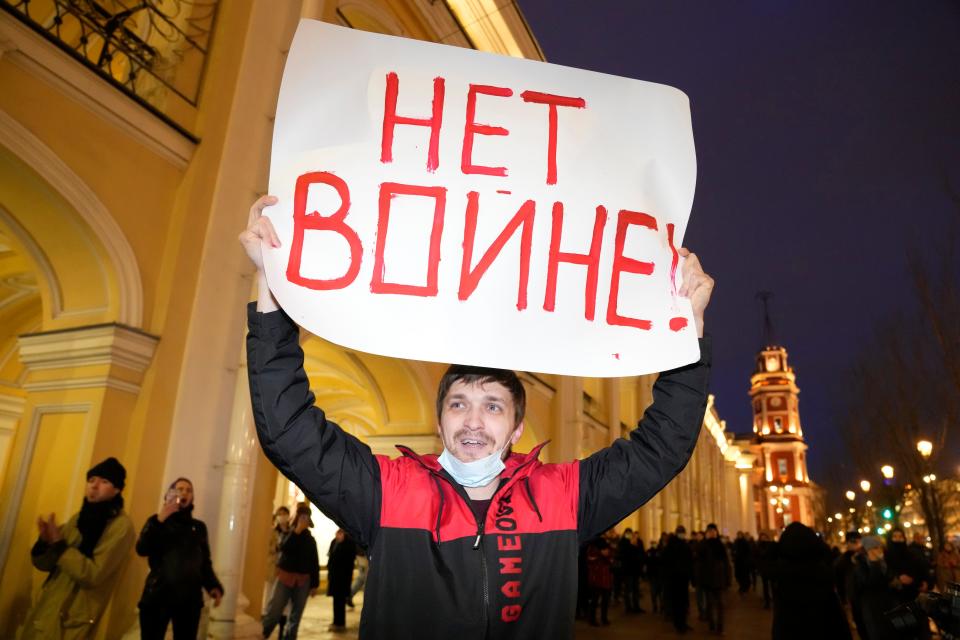 A man holds a sign that says "No War" in Russian.