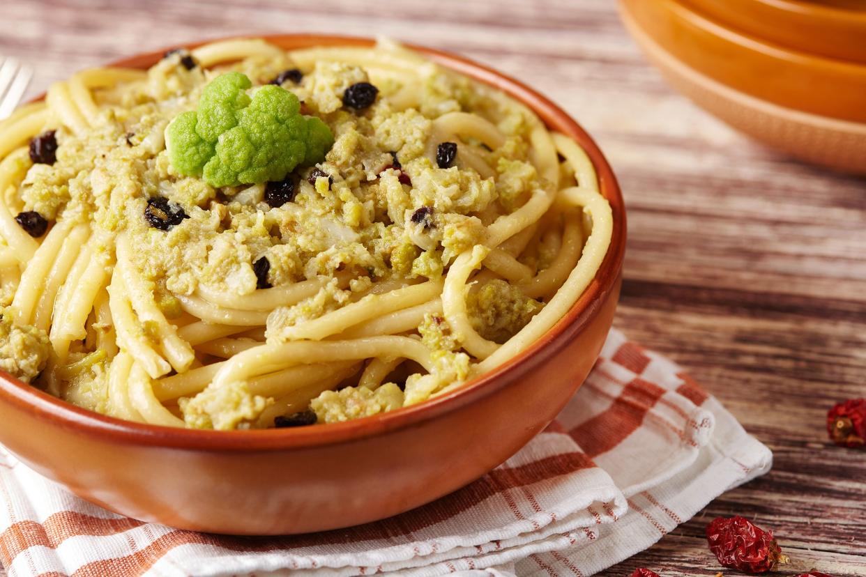 Bucatini with cauliflower and brussels sprouts in a terracotta bowl on a white and terracotta napkin on a wooden table with terracotta bowls in the background