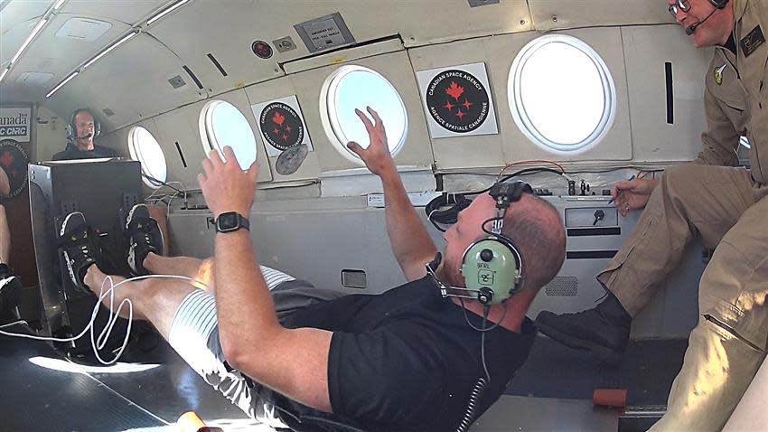  A person lying down in an airplane with their feet on the plate of a flywheel. their hands float, suggesting they are in microgravity during a parabolic flight. 