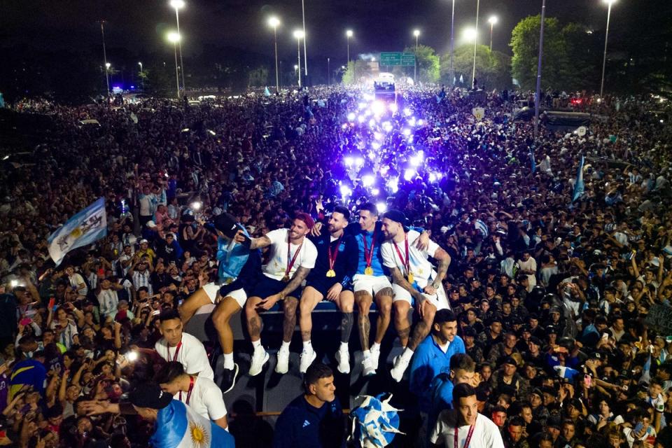 Argentina captain and striker Lionel Messi (C) holds the FIFA World Cup trophy aboard a bus as he celebrates alongside teammates and supporters (AFP via Getty Images)