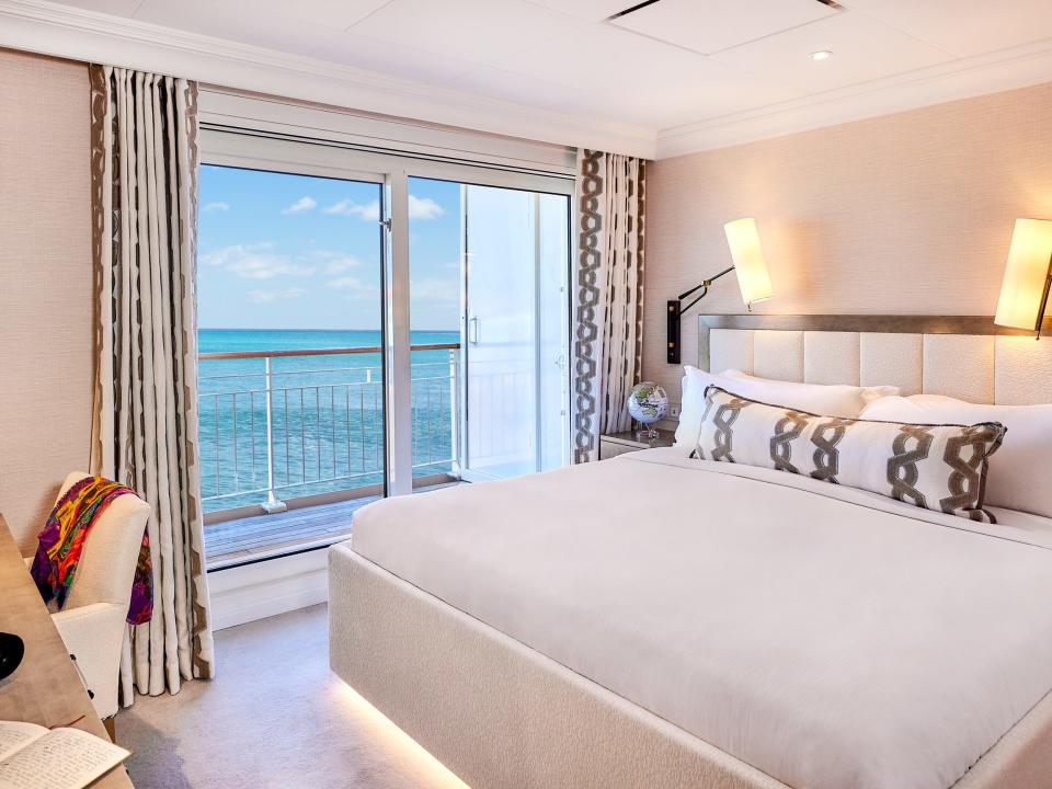 A bedroom in The World that has a window leading to a balcony looking out over the sea.