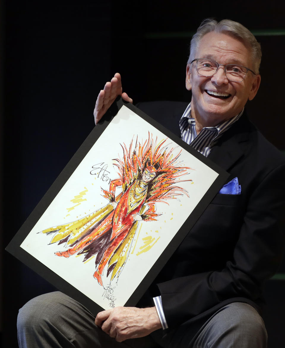 Fashion and Costume Designer Bob Mackie poses with one of his illustrations, a marker and pencil costume sketch of Elton John as a devil for his 1986 Ice on Fire tour, in London, Thursday, Aug. 16, 2018. The sketch which is signed by Bob is estimated at 1,000-2,000 US Dollars (788-1,575 UK Pounds) and will be auctioned in the 'Property from the Collection of Bob Mackie' sale by Julien's Auctions in Los Angeles on Nov. 17. (AP Photo/Kirsty Wigglesworth)