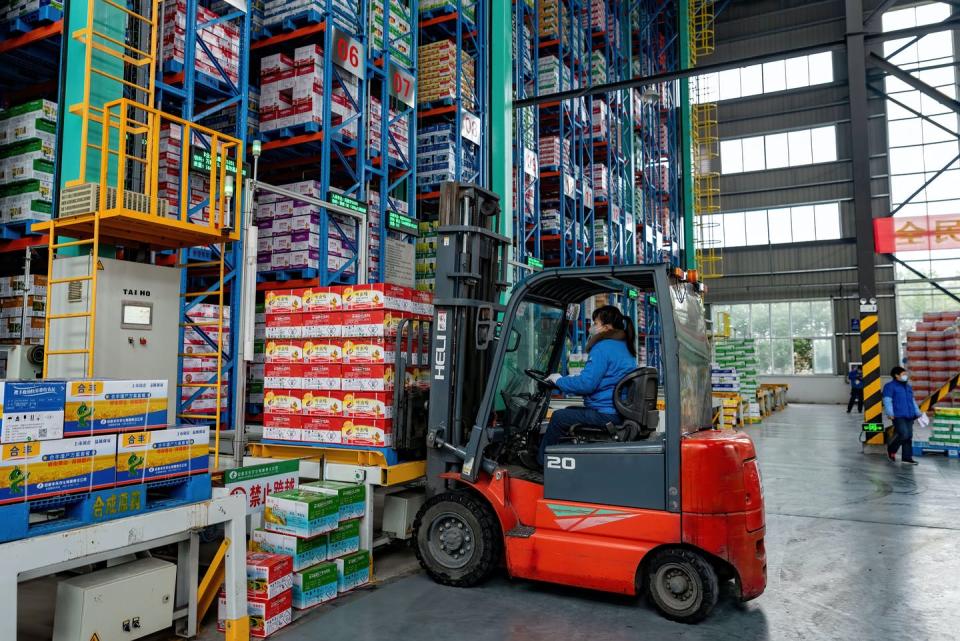 Man driving forklift loads pallets onto warehouse shelves.