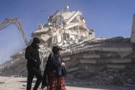 Local residents walk in front of a destroyed building in Nurdagi, southeastern Turkey, Thursday, Feb. 9, 2023. Thousands who lost their homes in a catastrophic earthquake huddled around campfires and clamored for food and water in the bitter cold, three days after the temblor and series of aftershocks hit Turkey and Syria. (AP Photo/Petros Giannakouris)