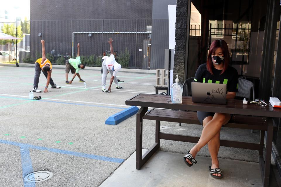 Operations Director Vienna Luu checks people in at an outdoor desk as instructor Joe Brown starts a dance class.