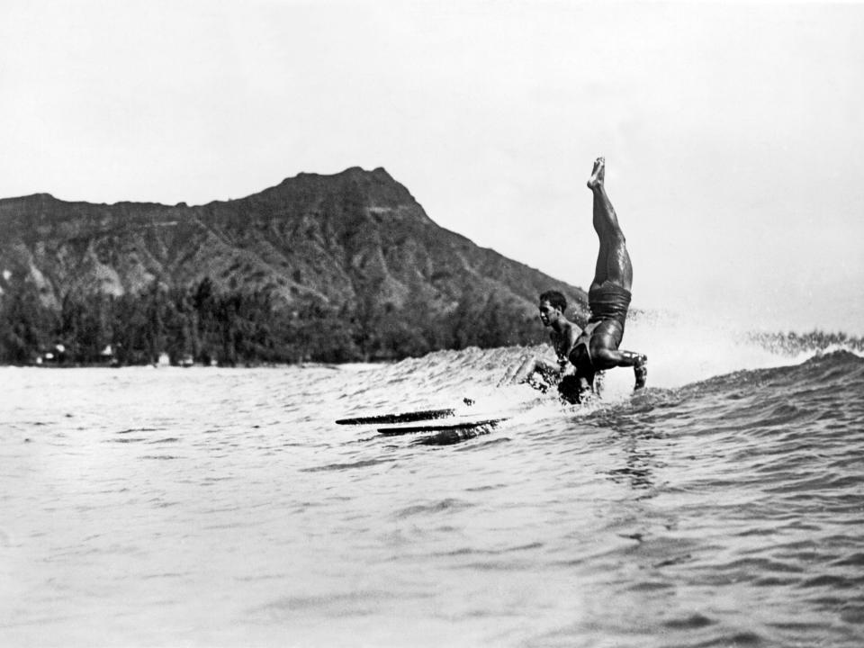 A surfer at Waikiki Beach stands on his head as he rides a wave into the shore, Honolulu, Hawaii, circa 1925. Diamond Head is in the background