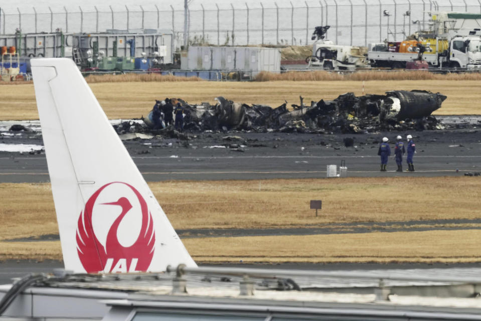 The burn-out Japanese coast guard aircraft is seen at rear behind the logo of Japan Airline at Haneda airport on Wednesday, Jan. 3, 2024, in Tokyo, Japan. Transport officials and police each began their on site investigation at Tokyo’s Haneda Airport on Wednesday after a large passenger plane and the Japanese coast guard aircraft collided on the runway and burst into flames, killing several people aboard the coast guard plane. (Kyodo News via AP)