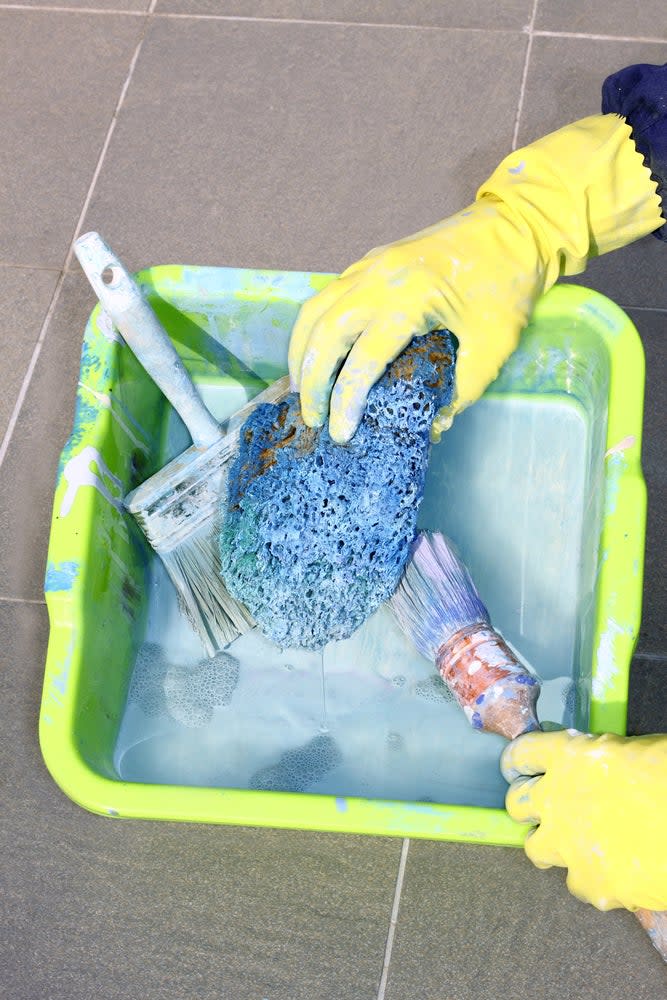 Washing used paint brushes with gloves in bucket of soapy water using a sponge. 