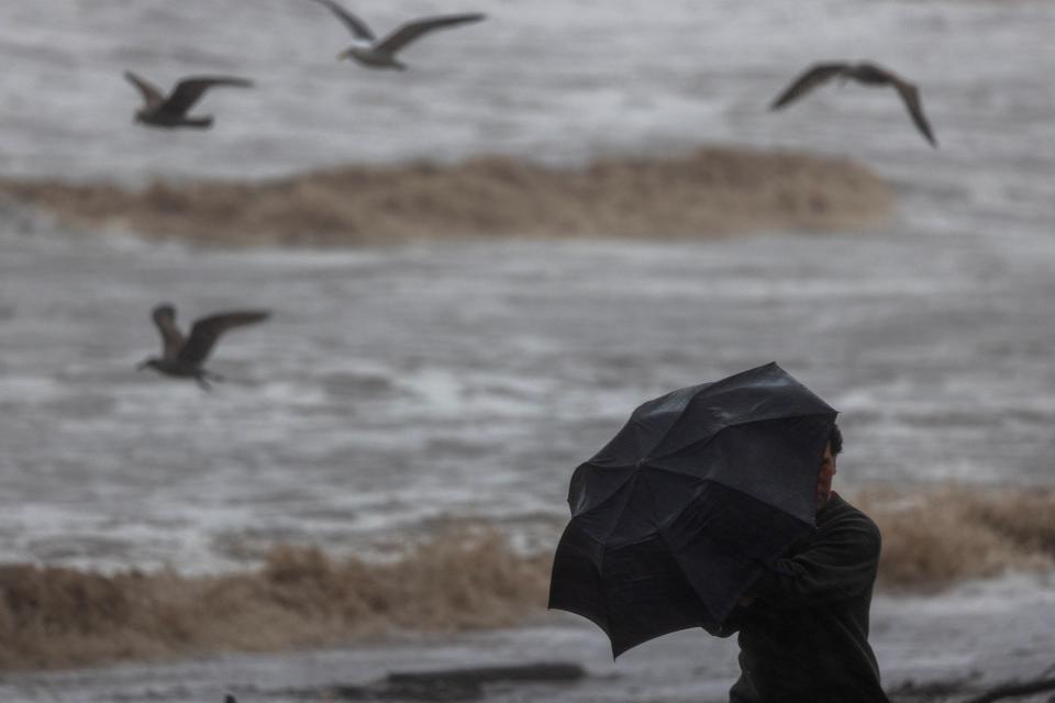 A man aims his umbrella into the wind near ocean surf turned mud brown by storm runoff water as the second and more powerful of two atmospheric river storms, and potentially the biggest storm of the season, arrives to Santa Barbara, California, on February 4, 2024. The US West Coast was getting drenched on February 1 as the first of two powerful storms moved in, part of a u0022Pineapple Expressu0022 weather pattern that was washing out roads and sparking flood warnings. The National Weather Service said u0022the largest storm of the seasonu0022 would likely begin on February 4.
