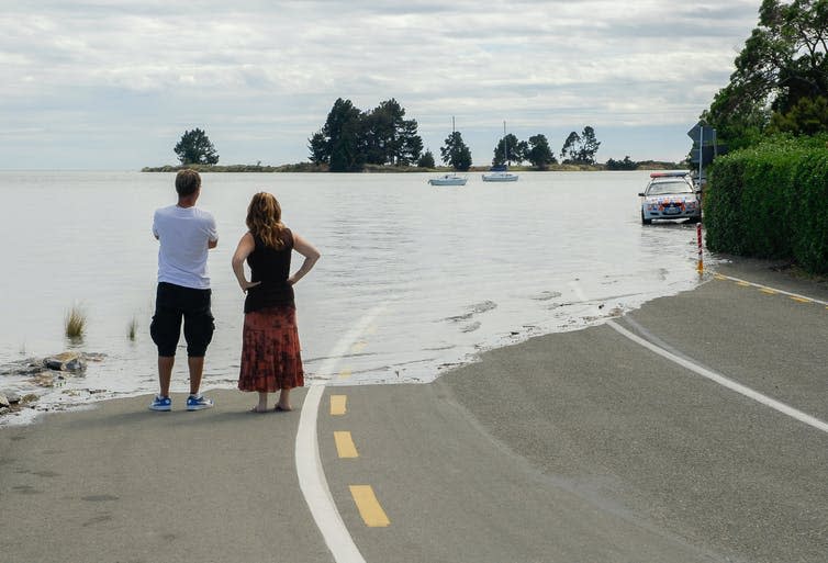 Two people look on as a motorway is engulfed by ocean water.