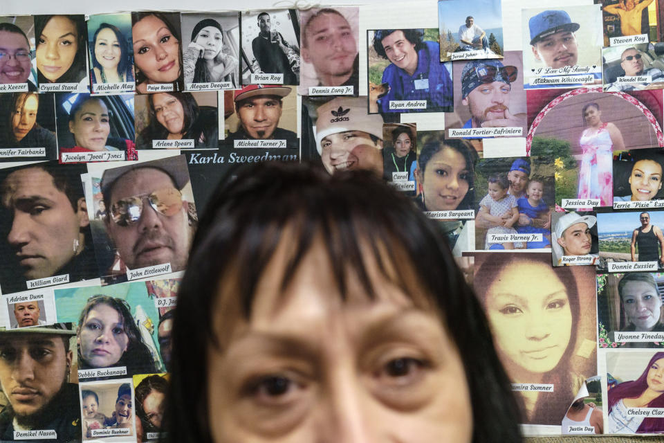 Terri Farley, who works with women at the Northwest Indian Community Development Center, sits in front of a posterboard pasted with 49 faces, a collage of their dead to drugs, Tuesday, Nov. 16, 2021, in Bemidji, Minn. She sees firsthand the pain addiction is causing in her community. They help people who've lost their children to the foster system, who'd been forced into prostitution, who face racism from law enforcement or landlords, who have no homes and no coats in the region's unforgiving winters. Farley can point out a half-dozen people she knows on the board. (AP Photo/David Goldman)