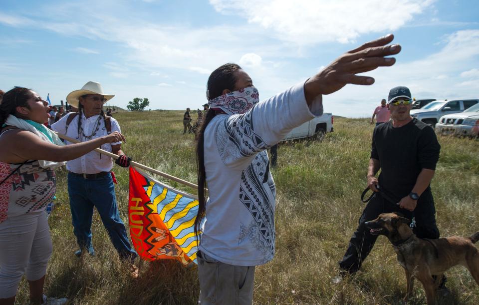 A Native American protestors holds up his arms as he and other protestors are threatened by private security guards and guard dogs.