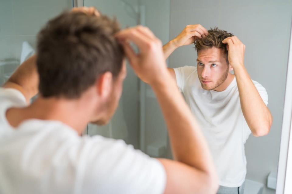 young man in white t-shirt and jeans looking in the mirror thinning hair