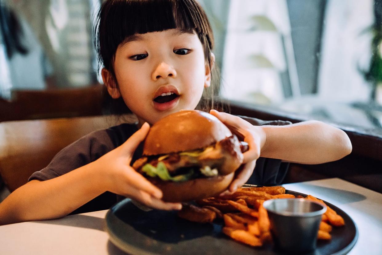 A child holds a gourmet burger at a restaurant