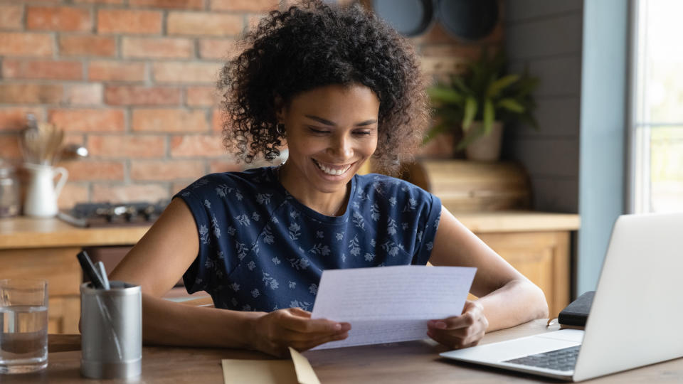 A woman smiling at her desk with a piece of paper in her hand