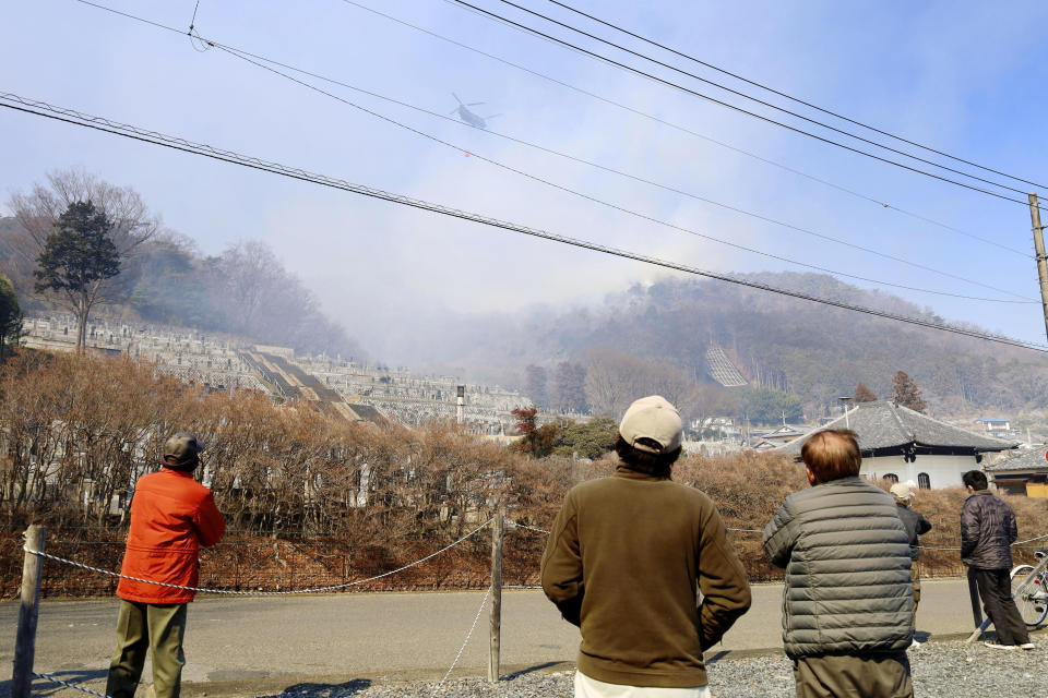 Residents watch as a helicopter dumps water on a wildfire in Ashikaga, Tochigi prefecture, north of Tokyo Wednesday, Feb. 24, 2021. A forest fire broke out in the rural area Thursday, near another blaze burning since Sunday, Feb. 21. (Kyodo News via AP)