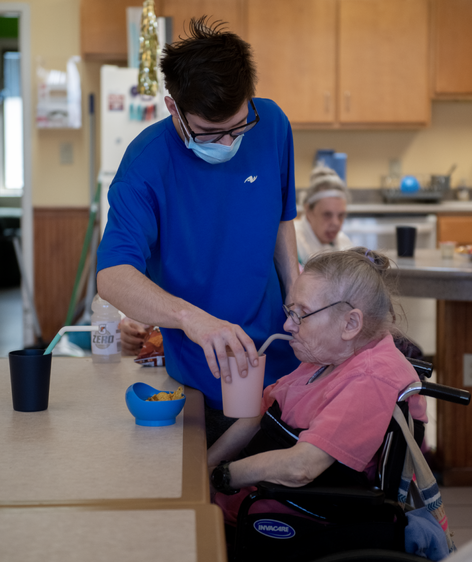 Direct support professional Corey Austin helps Kathy Gainer with her drink.