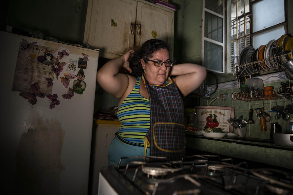 Yuliet Colon puts on her apron as she prepares to cook a dish in her kitchen in Havana, Cuba, Friday, April 2, 2021. Colon found for herself and many Cubans a solution that combines ingenuity with the innovative use of the Internet on the island and became a contributor to the Facebook page “Recipes from the Heart,” with tips, ideas and tricks to get ahead with what items are actually available at the market. (AP Photo/Ramon Espinosa)