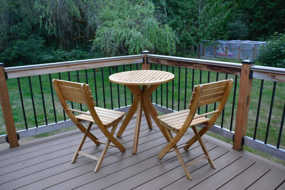 small wooden bistro set table and two folding chairs in corner of wooden deck