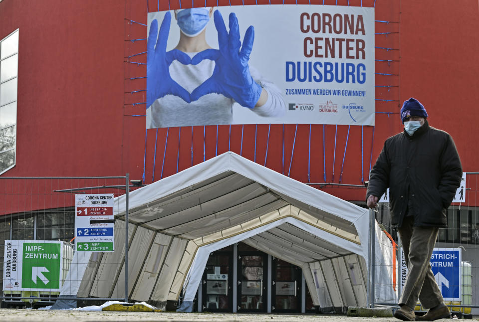 FILE - In this Monday, Jan. 25, 2021 file photo, a man wearing a face mask walks past the Corona Center in Duisburg, Germany. The former Musical theater has been turned into a COVID-19 test and vaccination center. Thousands of elderly Germans faced online error messages and jammed up hotlines Monday as technical problems marred the start of the coronavirus vaccine campaign for over-80s in the country's most populous state. (AP Photo/Martin Meissner, File)