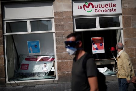 A masked protester walks in front of a vandalized office during a demonstration on Act 44 (the 44th consecutive national protest on Saturday) of the yellow vests movement in Nantes