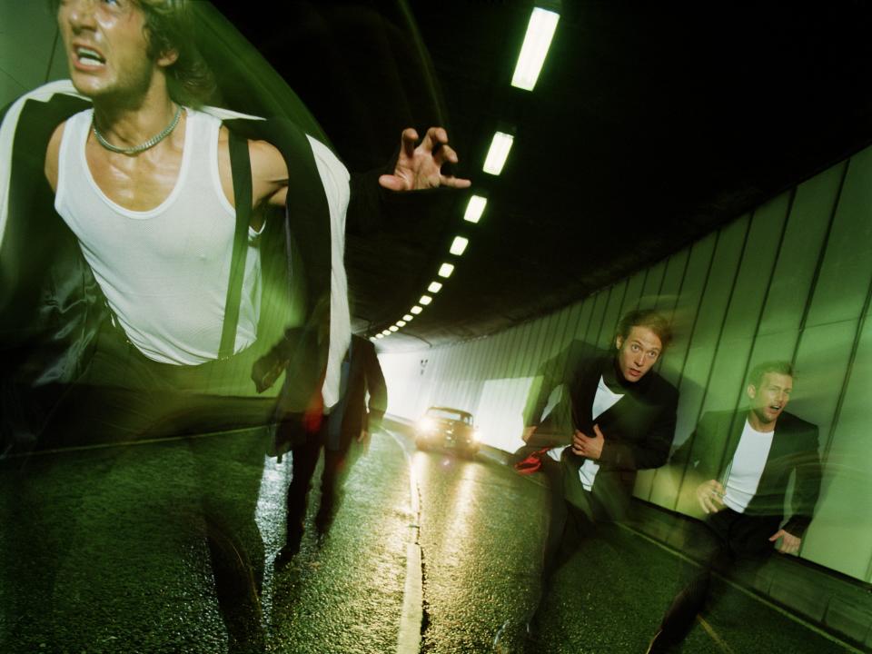 Four men running through tunnel, pursued by car (blurred motion) - stock photo